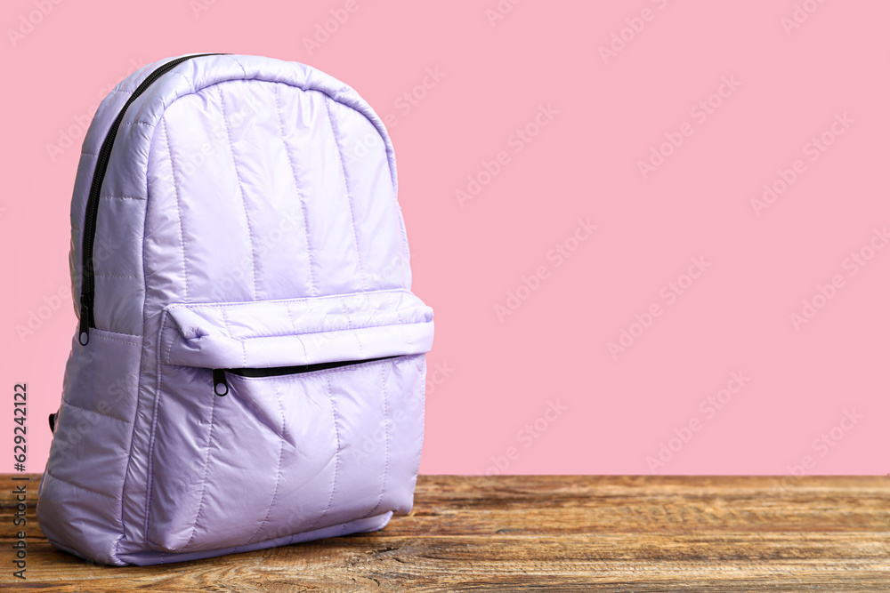 Lilac school backpack on wooden table near pink wall