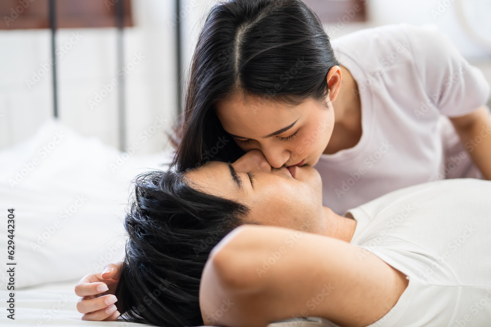 Asian wife kissing her husband while lying down sleep on bed in bedroom. 