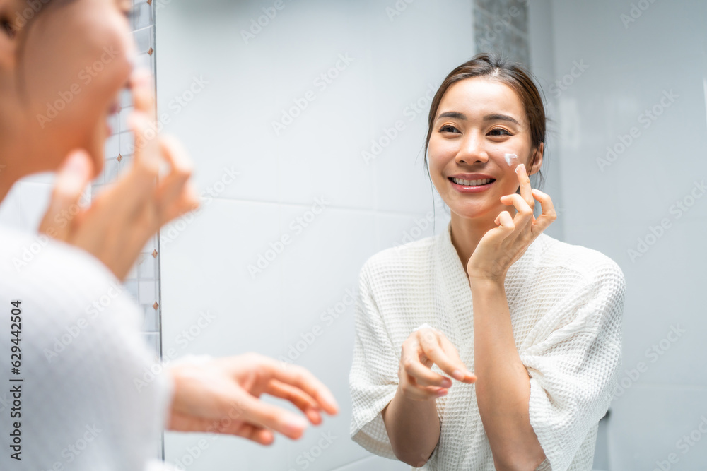 Asian beautiful woman looking at the mirror after apply lotion on face. 