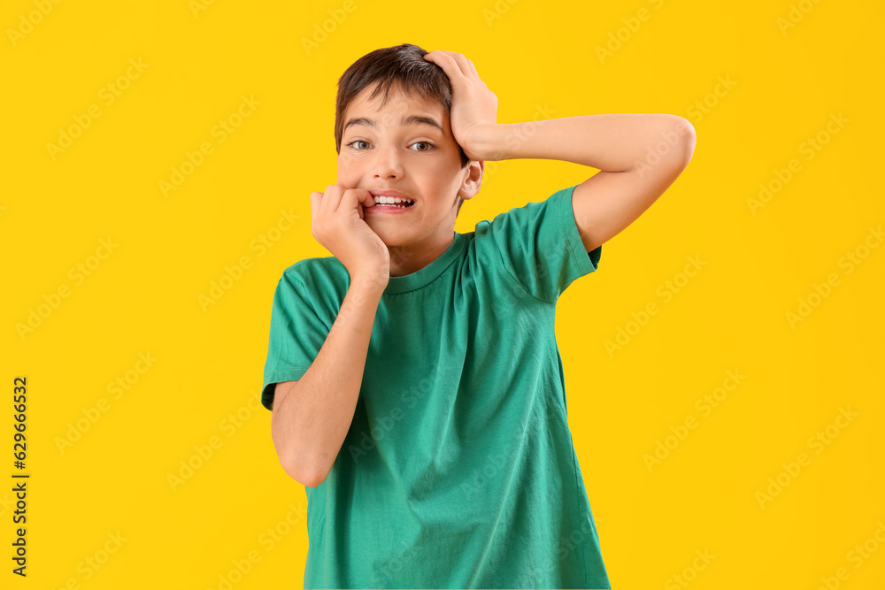 Little boy biting nails on yellow background