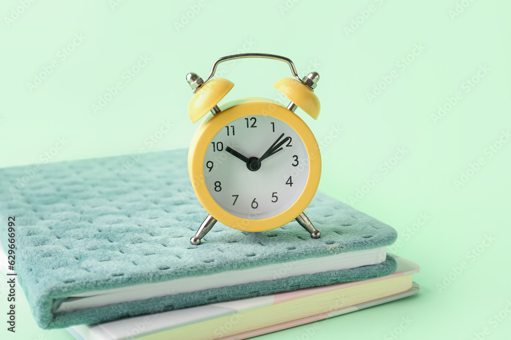 Notebooks and alarm clock on color background, closeup