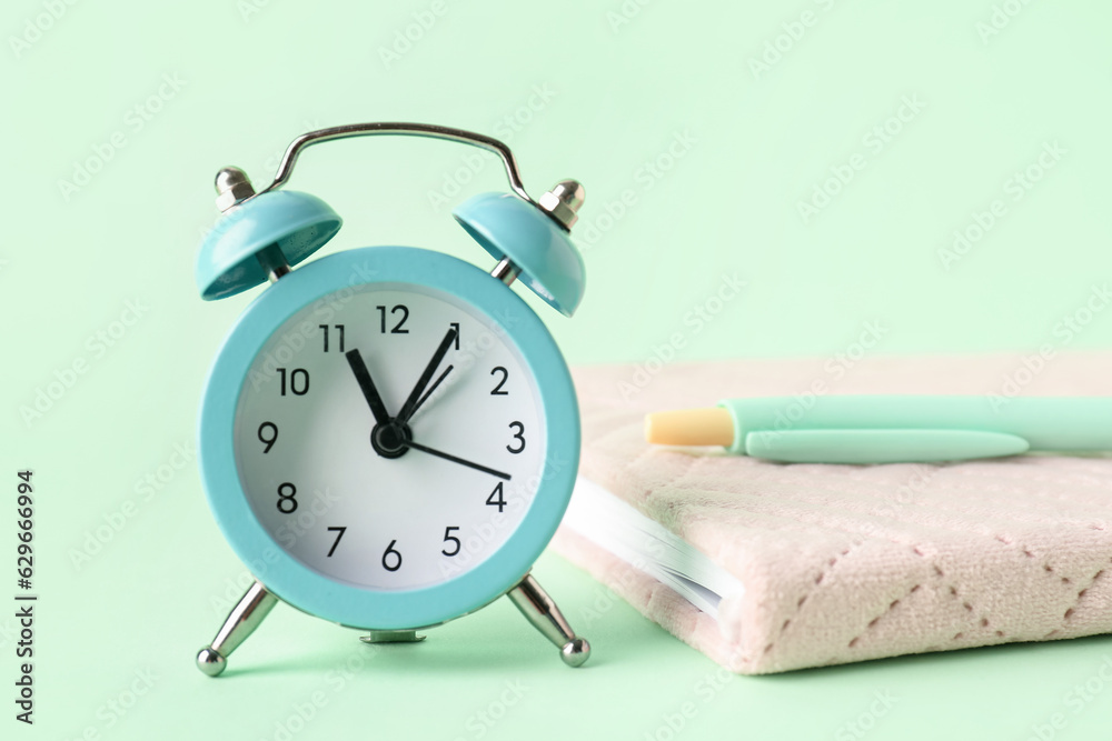 Alarm clock, pen and notebook on color background, closeup