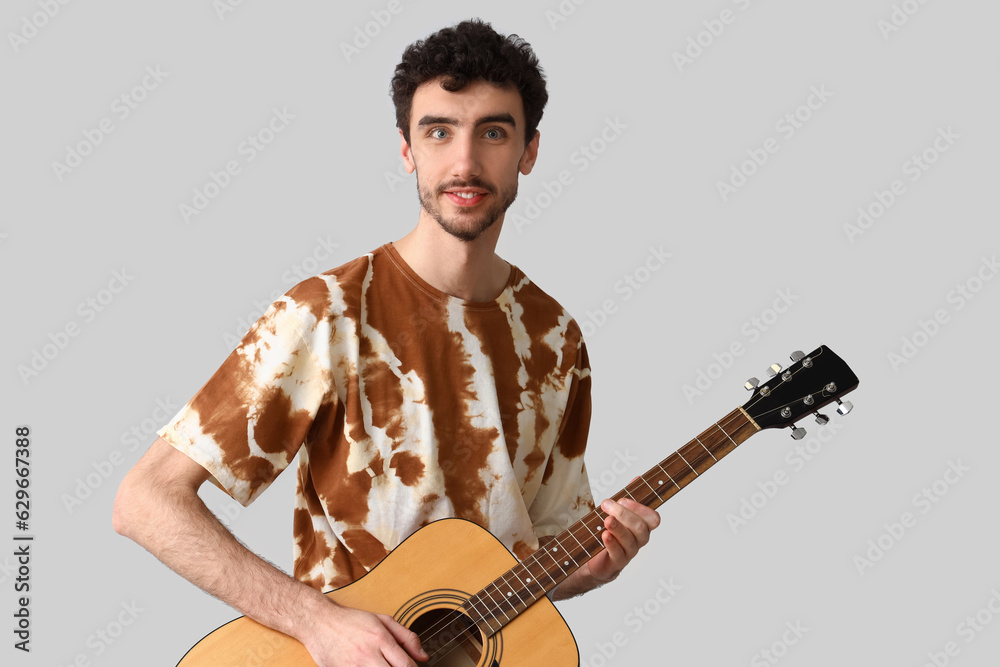 Handsome man in tie-dye t-shirt with guitar on light background