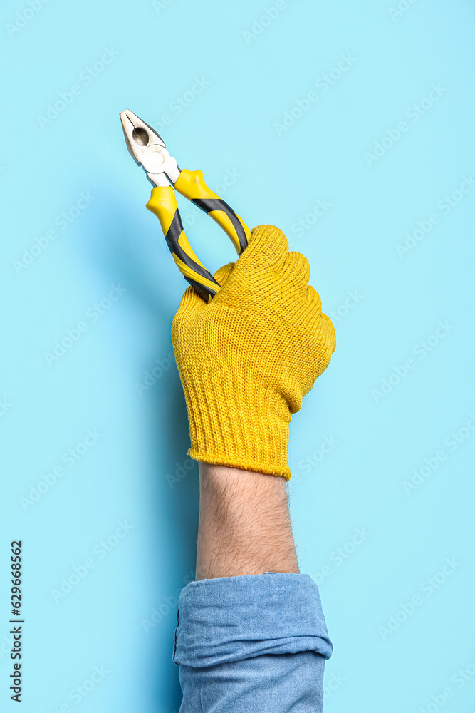 Male hand in gloves holding pliers on blue background