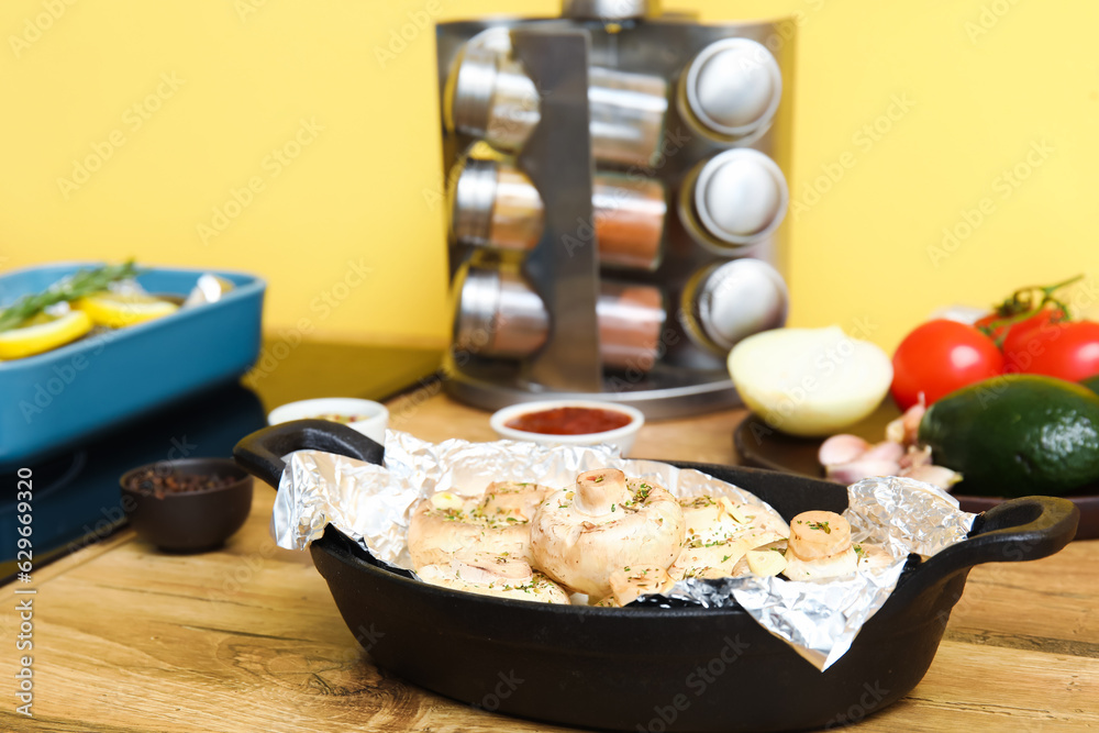 Baking dish with raw mushrooms, spices and vegetables on wooden table in kitchen