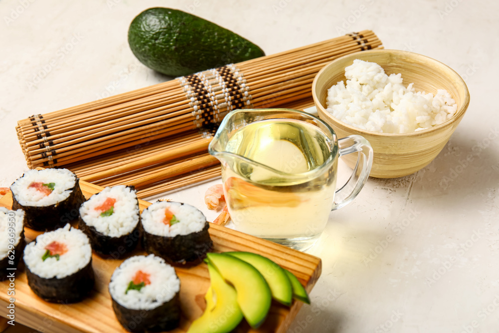 Wooden board with tasty sushi rolls, ingredients, bamboo mat and chopsticks on light background