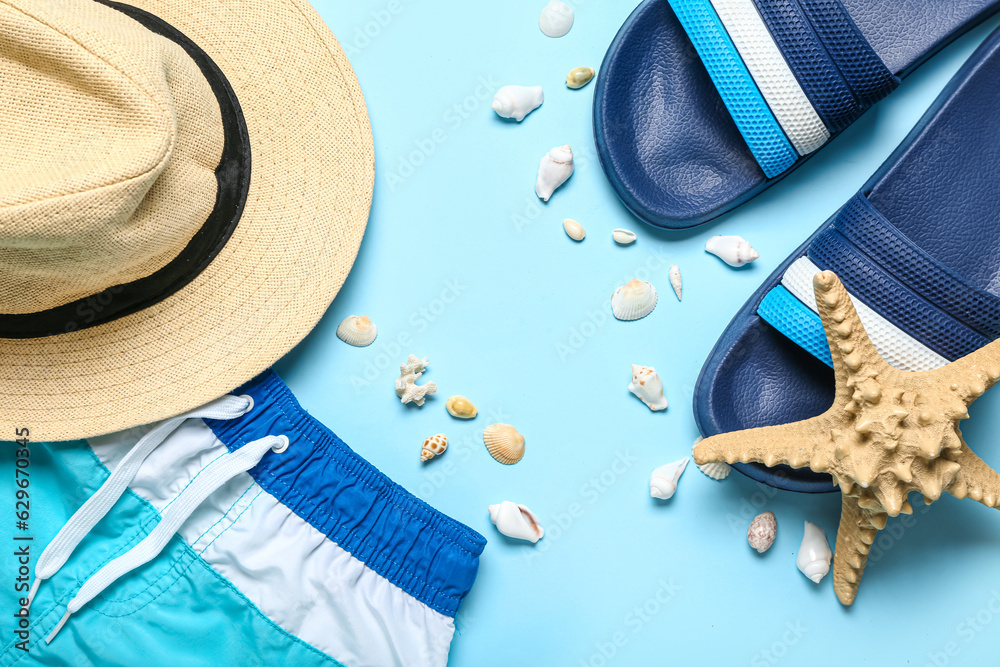 Flip-flops with seashells, hat and shorts on blue background