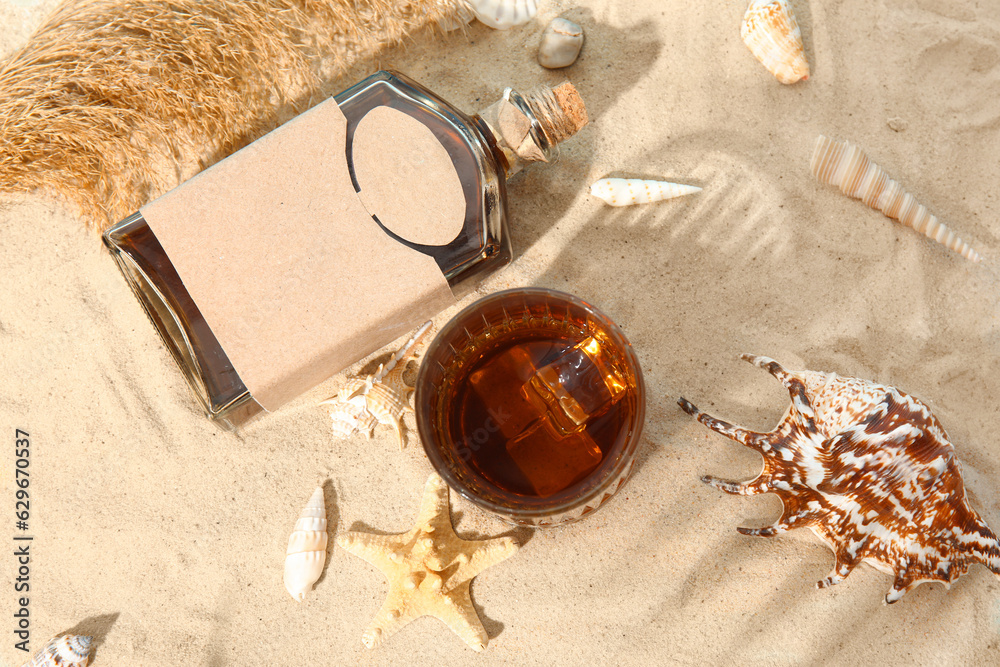 Composition with bottle and glass of cold rum on sand