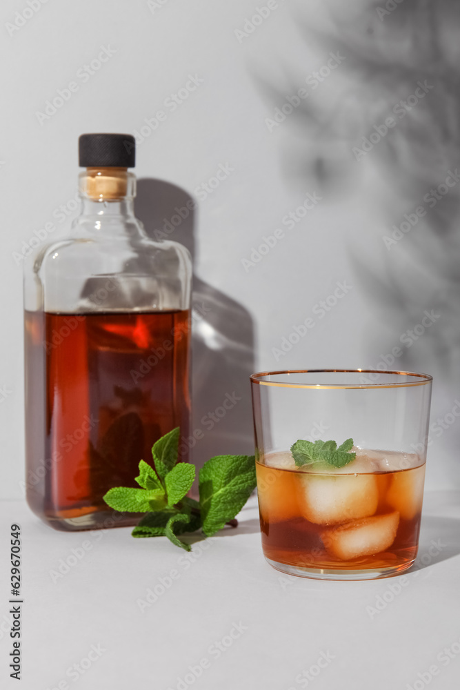 Bottle and glass of cold rum on grey background