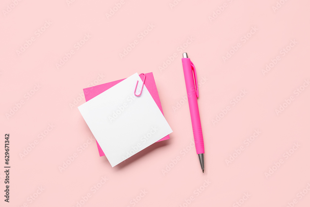 Sticky notes with paper clip and pen on pink background