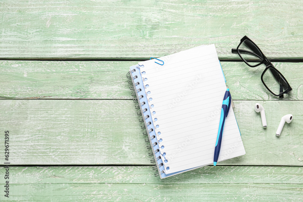 Composition with notepad, eyeglasses and earphones on green wooden background