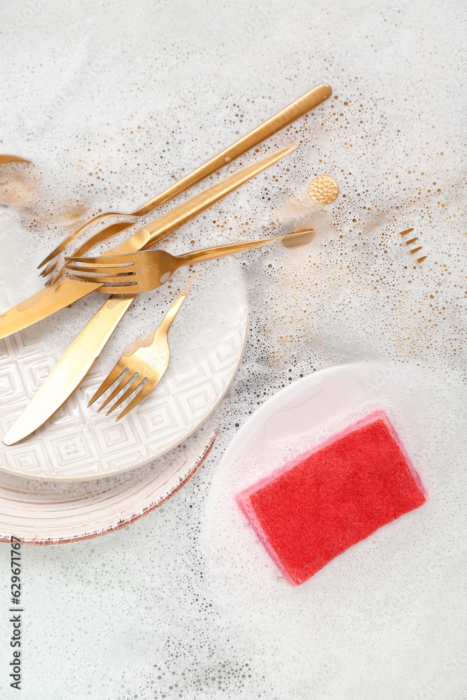 Cleaning sponge with dishes and foam in water, closeup