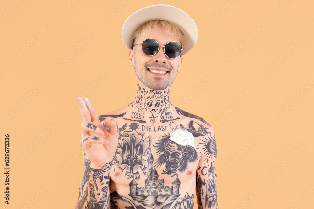 Tattooed man applying sunscreen cream on beige background