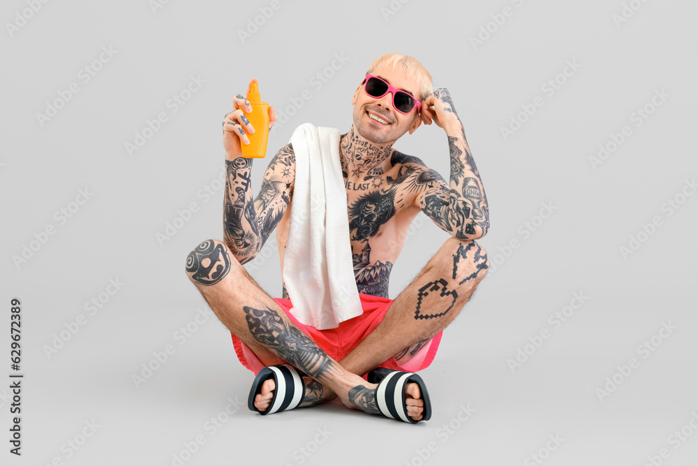 Tattooed man with sunscreen cream on light background