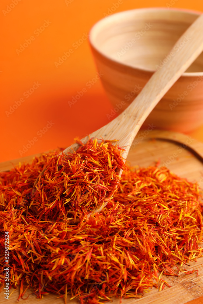 Wooden board and spoon with pile of saffron on orange background