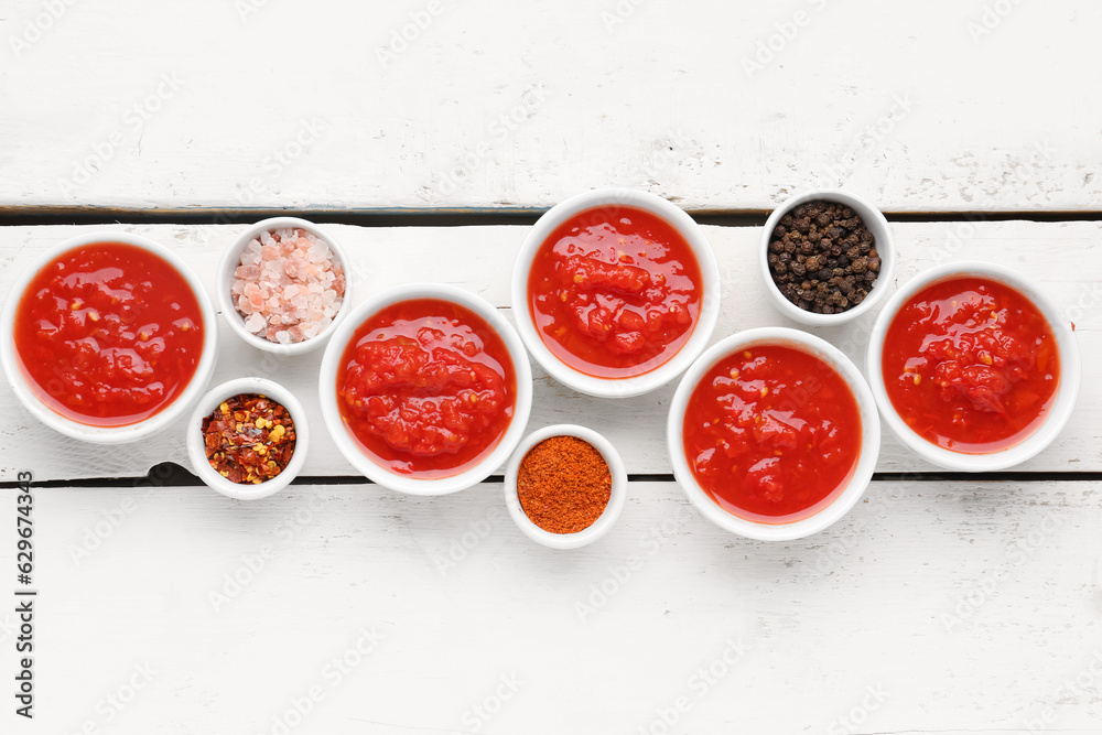 Bowls with tasty tomato sauce and ingredients on white wooden background