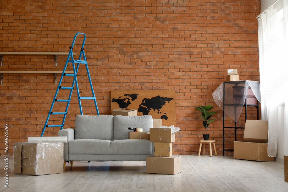 Sofa with cardboard boxes and ladder in living room on moving day