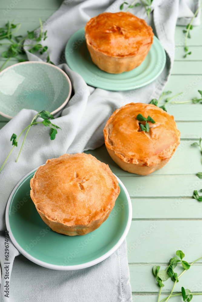 Plates with tasty meat pot pie on green wooden background