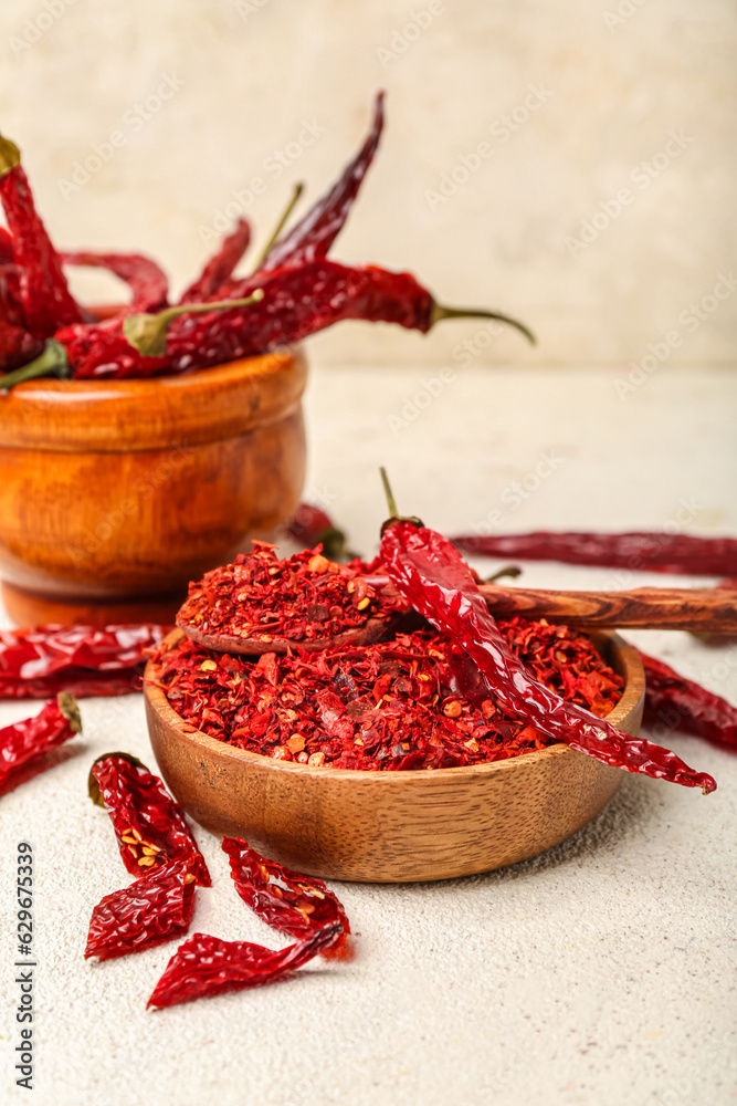 Composition with wooden bowl and mortar of dry hot chili peppers on white background