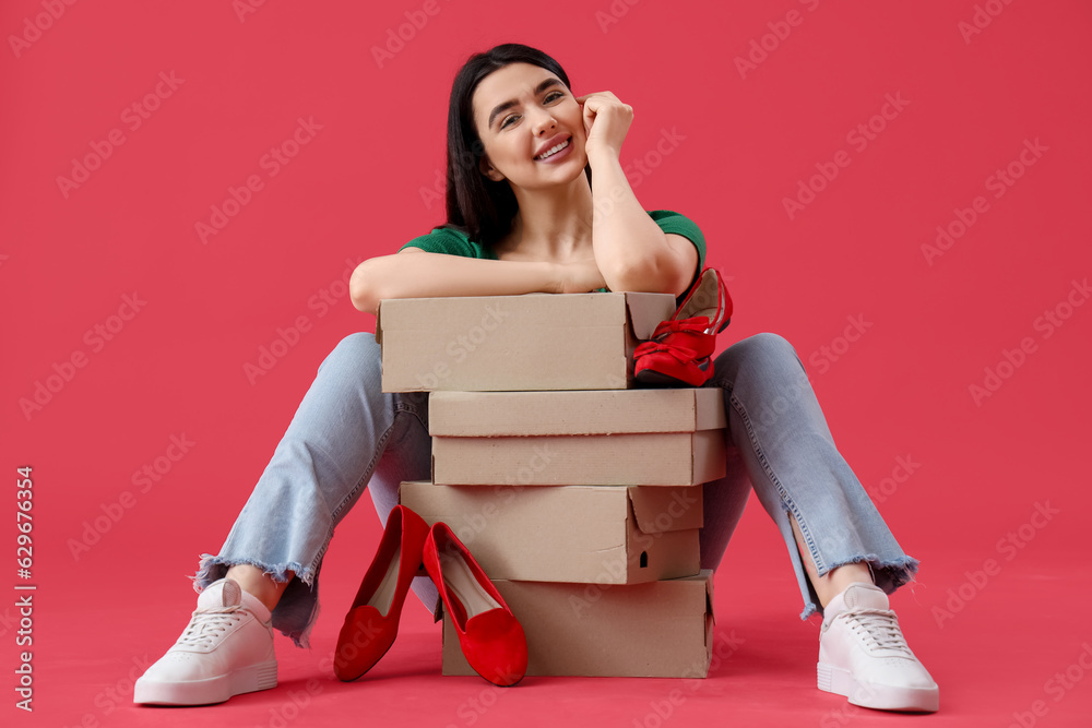 Young woman with shoe boxes sitting on red background