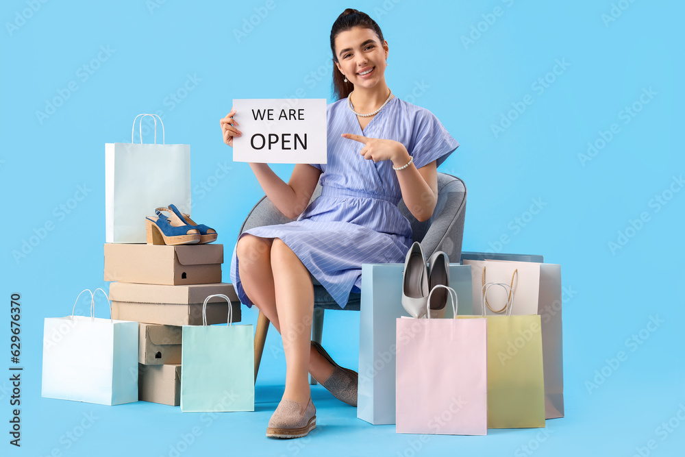 Female seller with opening sign, shoe boxes and shopping bags on blue background