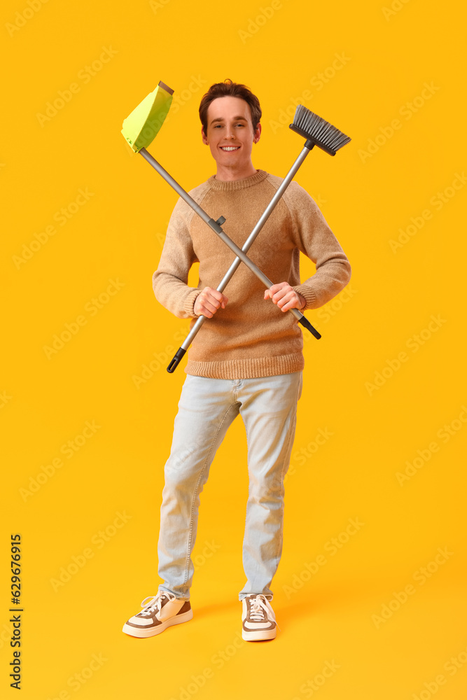 Young man with broom and dustpan on yellow background