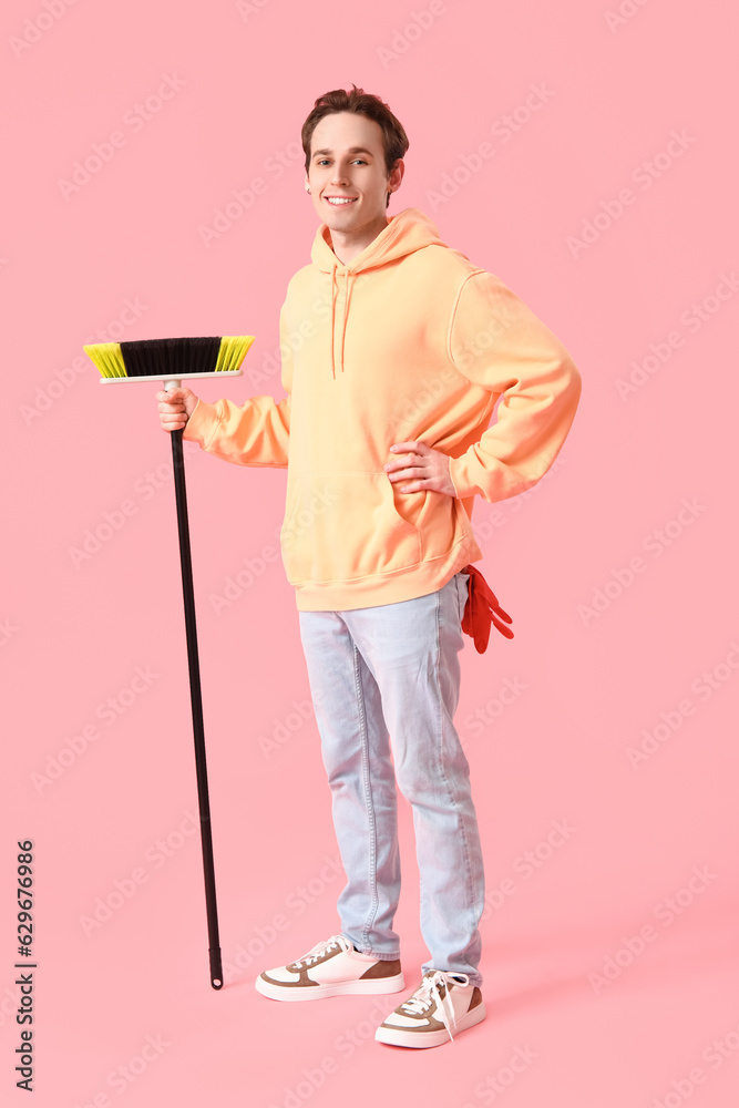 Young man with broom on pink background