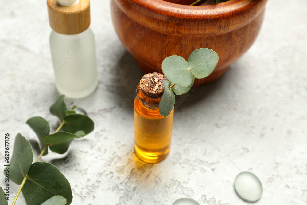 Cosmetic oil bottles with wooden mortar and pestle and eucalyptus branch on grey textured background