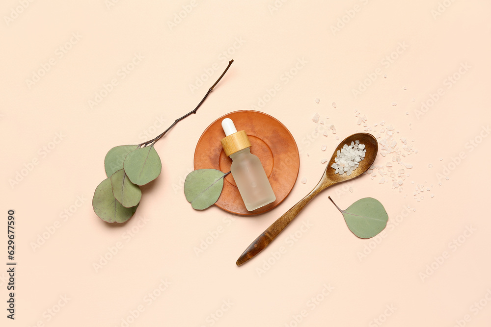 Bottle of cosmetic oil with sea salt and eucalyptus branch on beige background