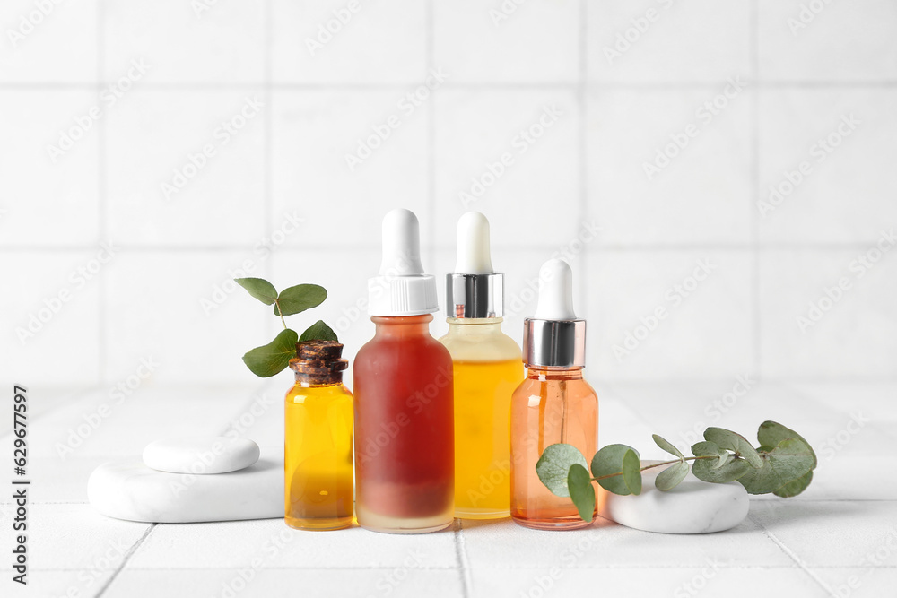 Composition with bottles of cosmetic oil, spa stones and eucalyptus branch on white tile