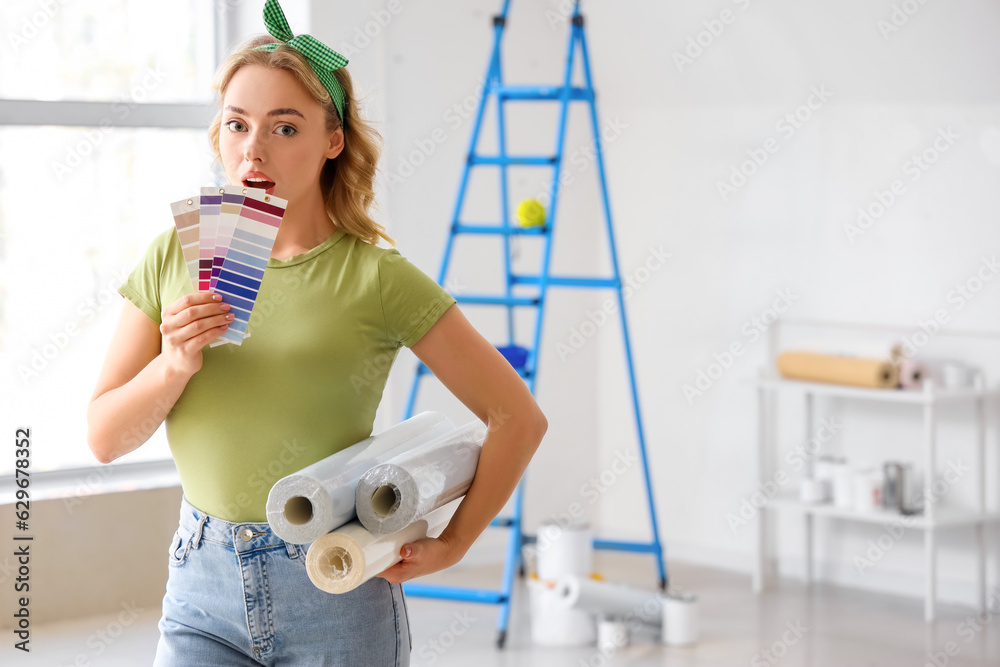 Young woman with wallpaper rolls and paint color palettes at home