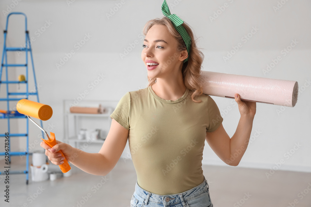 Young woman with wallpaper roll and paint roller at home