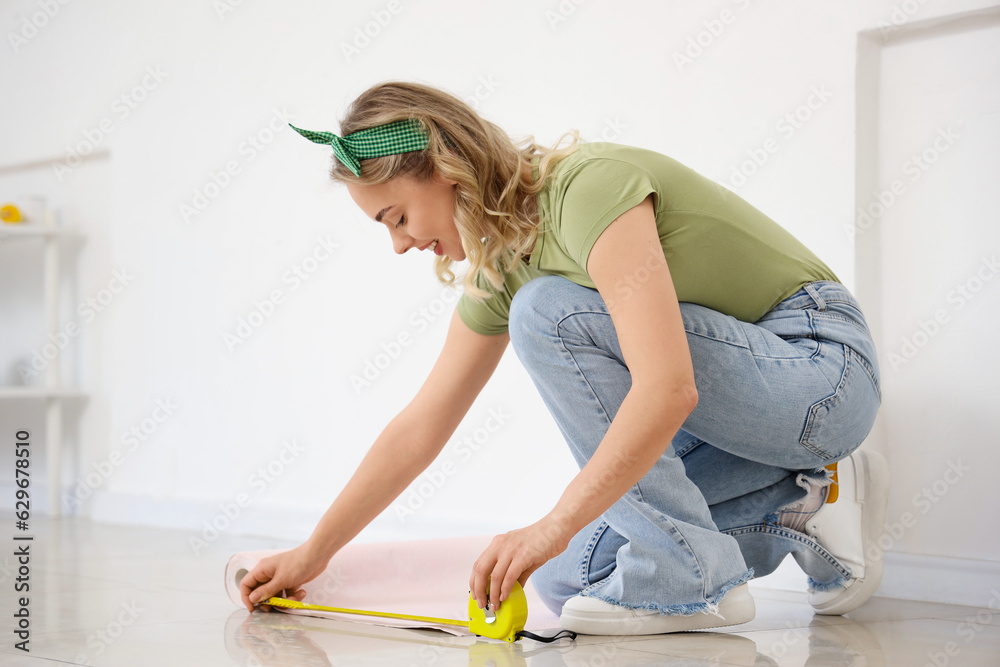 Young woman measuring wallpaper at home