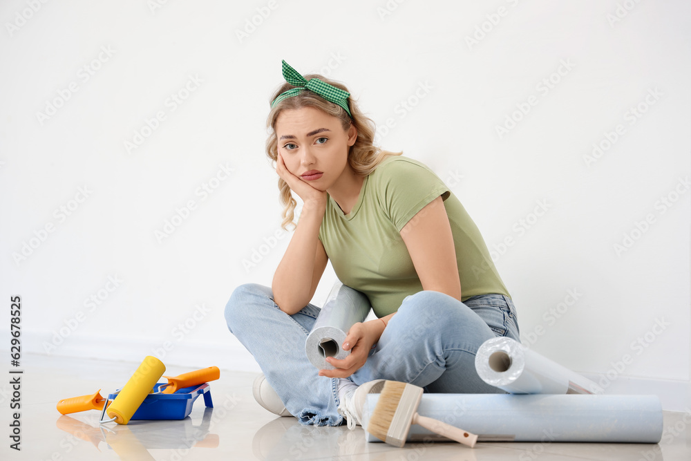 Upset young woman with wallpaper roll sitting at home