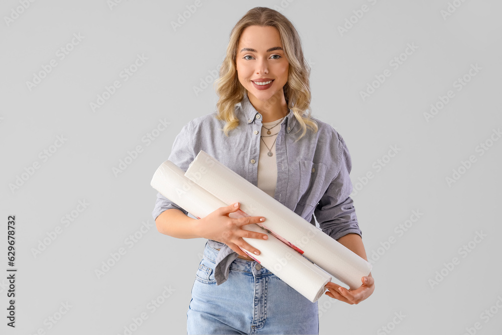 Young woman with wallpaper rolls on grey background