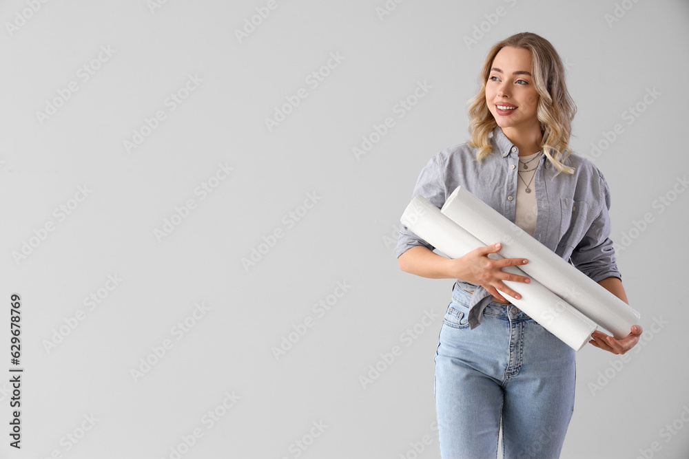 Young woman with wallpaper rolls on grey background