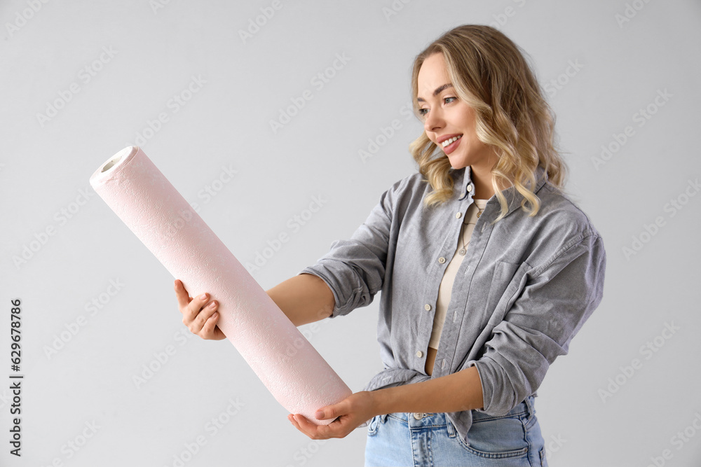 Young woman with wallpaper roll on grey background