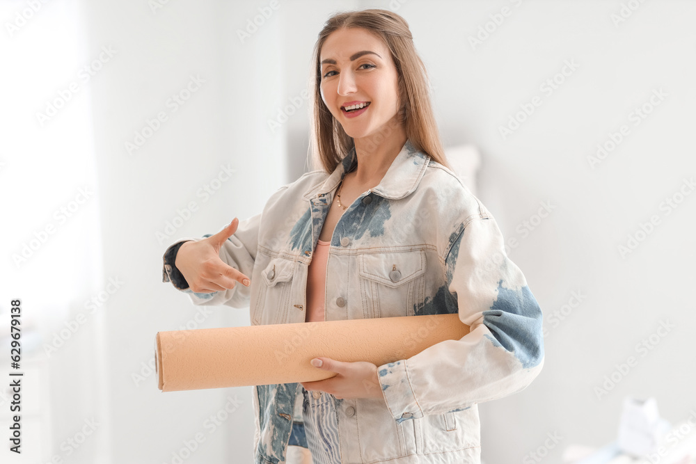 Young woman pointing at wallpaper roll in room