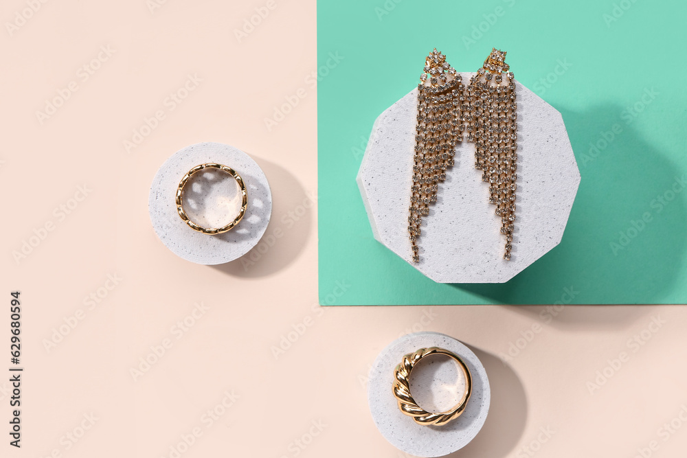 Decorative podiums with golden rings and earrings on color background