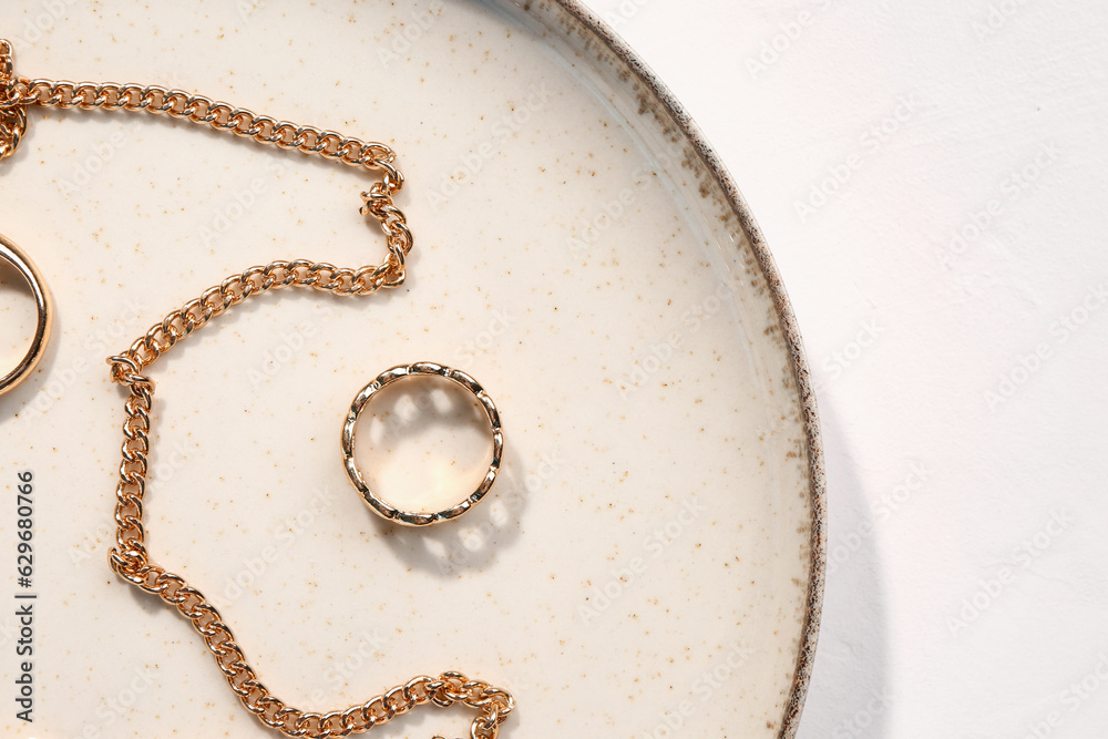 Plate with golden rings and necklace on white background