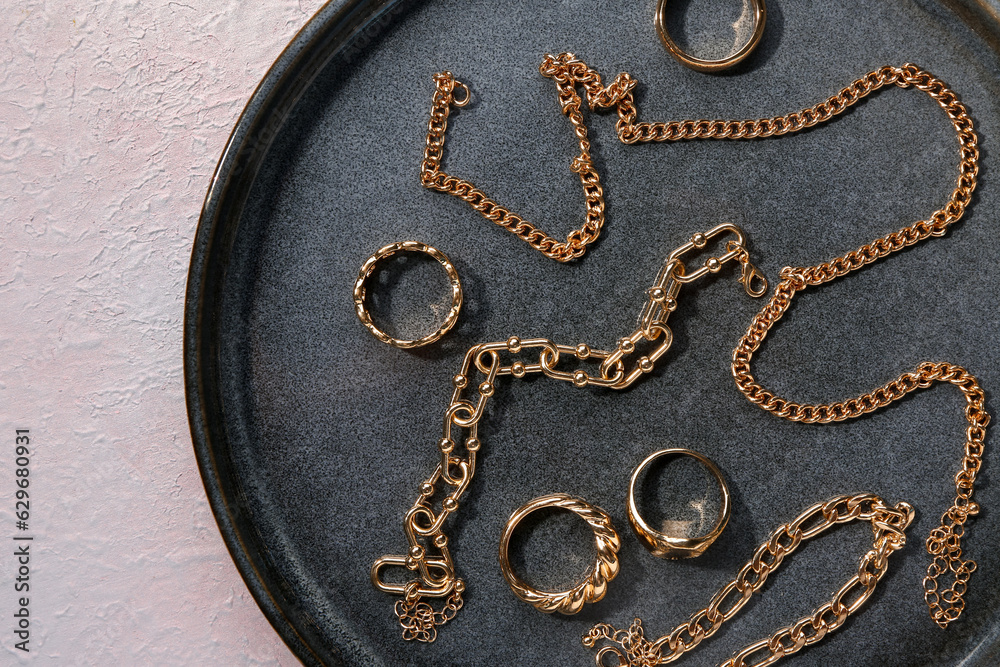 Plate with beautiful golden jewellery on pink textured background