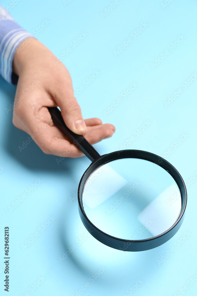 Female hand with magnifier on blue background