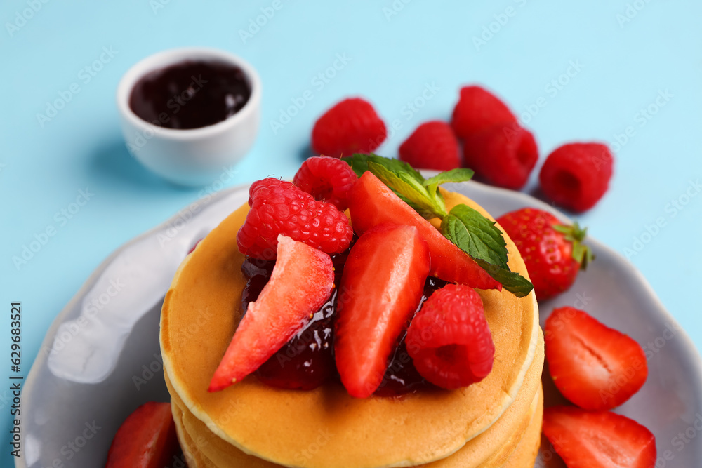 Plate with sweet pancakes, berries and jam on blue background, closeup