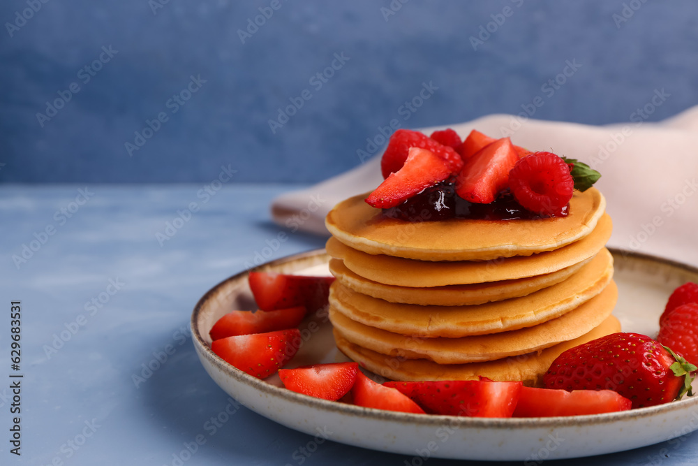 Plate with tasty pancakes and berries on blue background, closeup