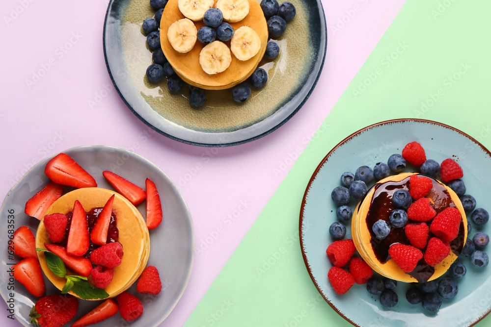 Plates with sweet pancakes and berries on color background