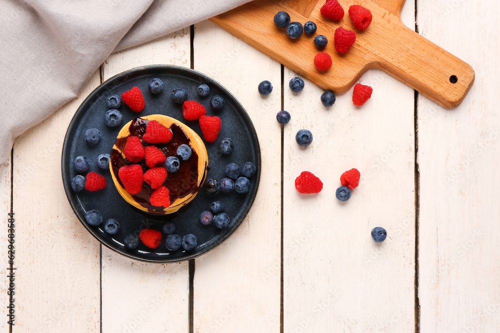 Plate with sweet pancakes and berries on light wooden background