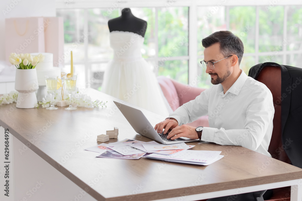 Male wedding planner working with laptop in office