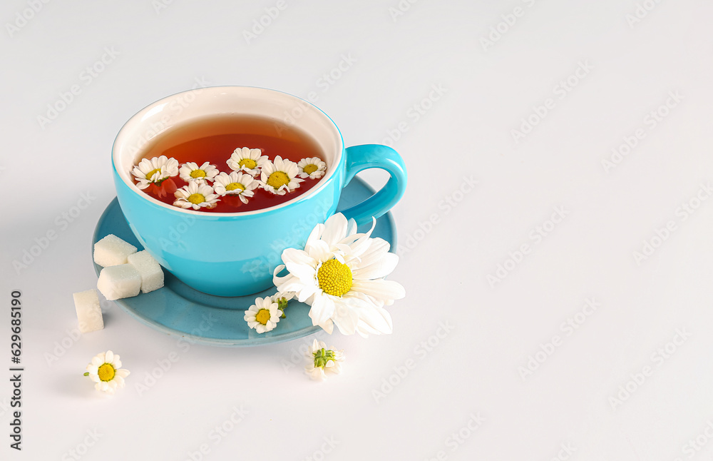 Cup of natural chamomile tea and flowers on white background