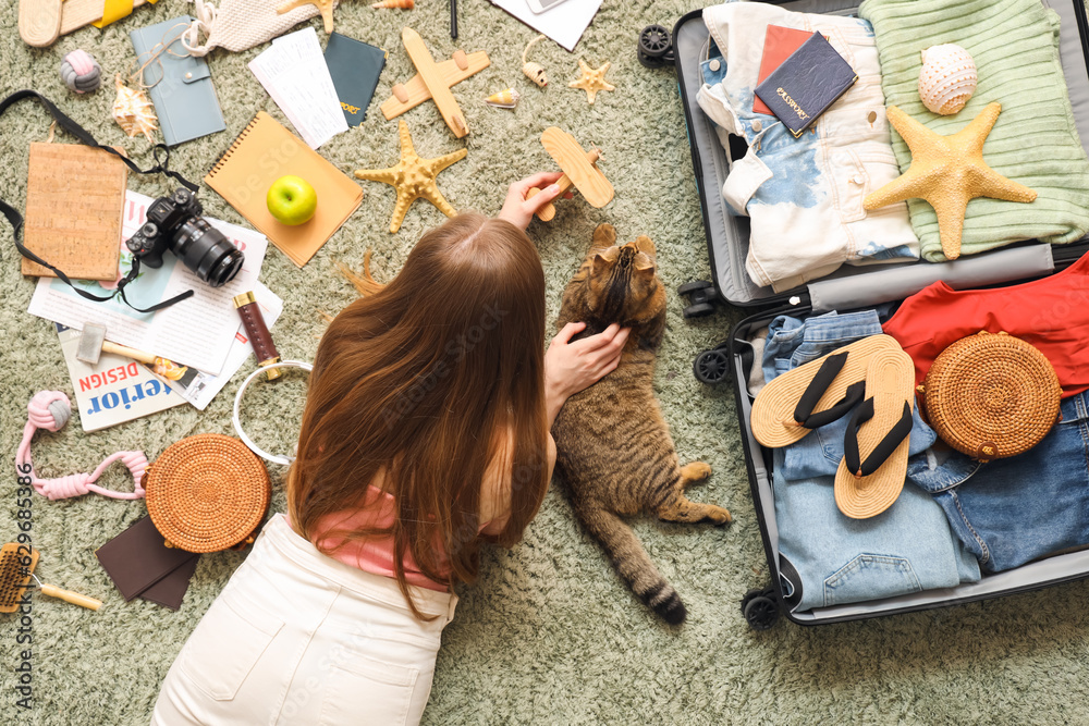 Woman with Scottish fold cat and travelling accessories on green carpet, top view