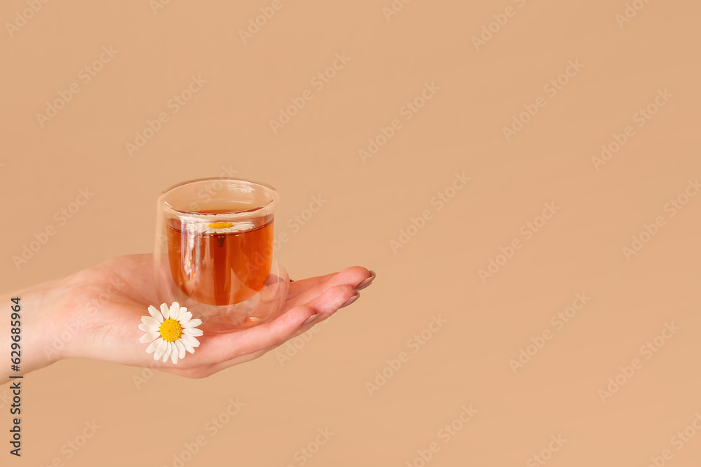 Female hand with cup of chamomile tea near beige wall